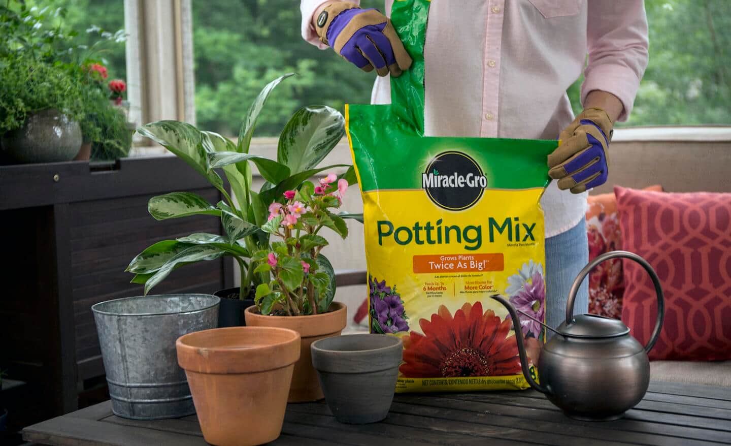 A bag of potting mix sits next to some plants and pots.