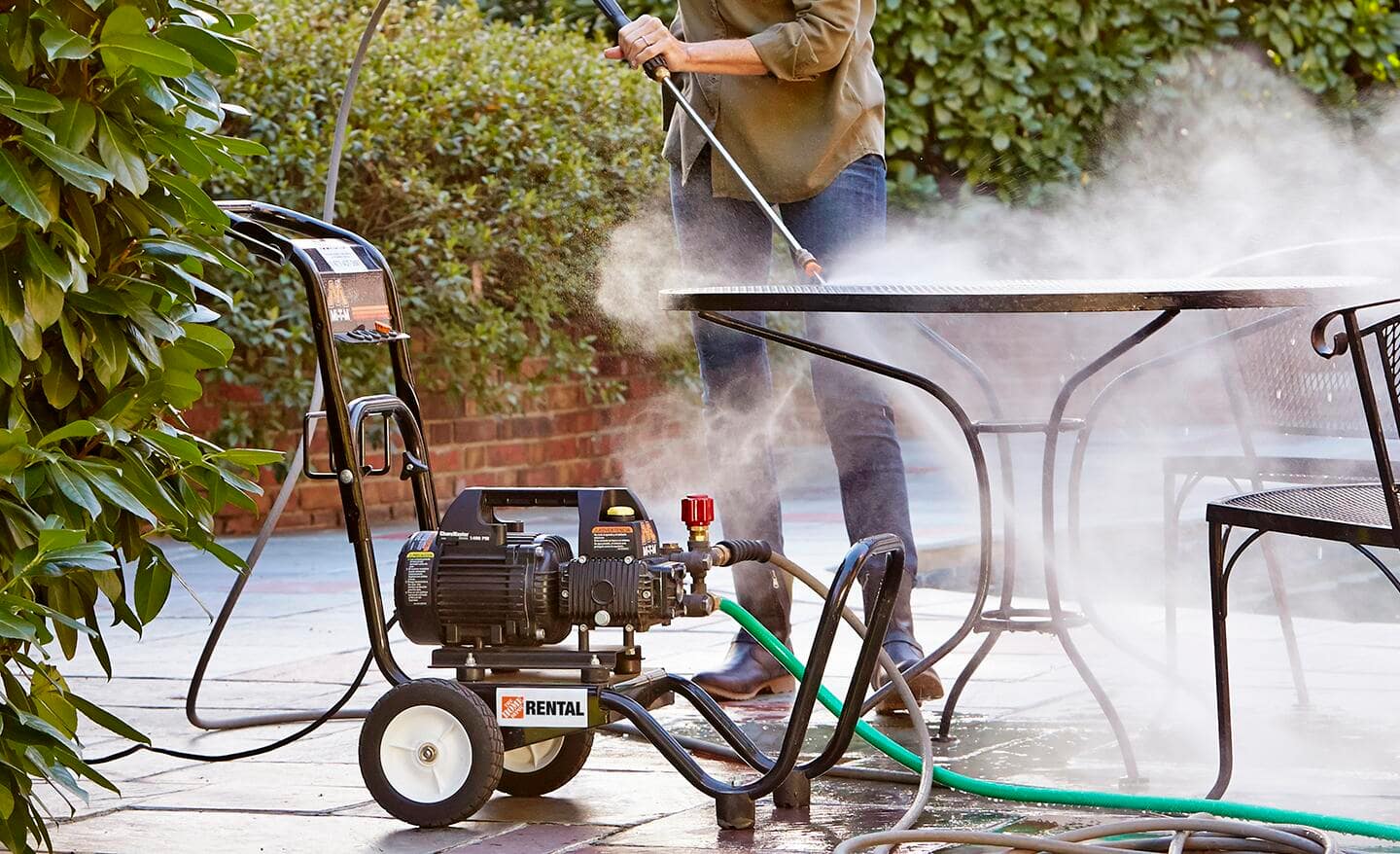 A woman using an electric pressure washer on patio table.