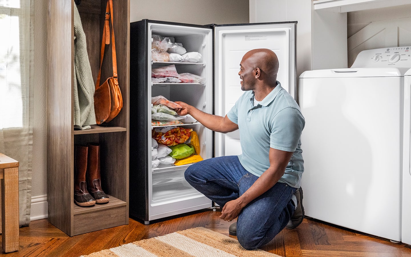 A man getting frozen food from an upright freezer in a mudroom.