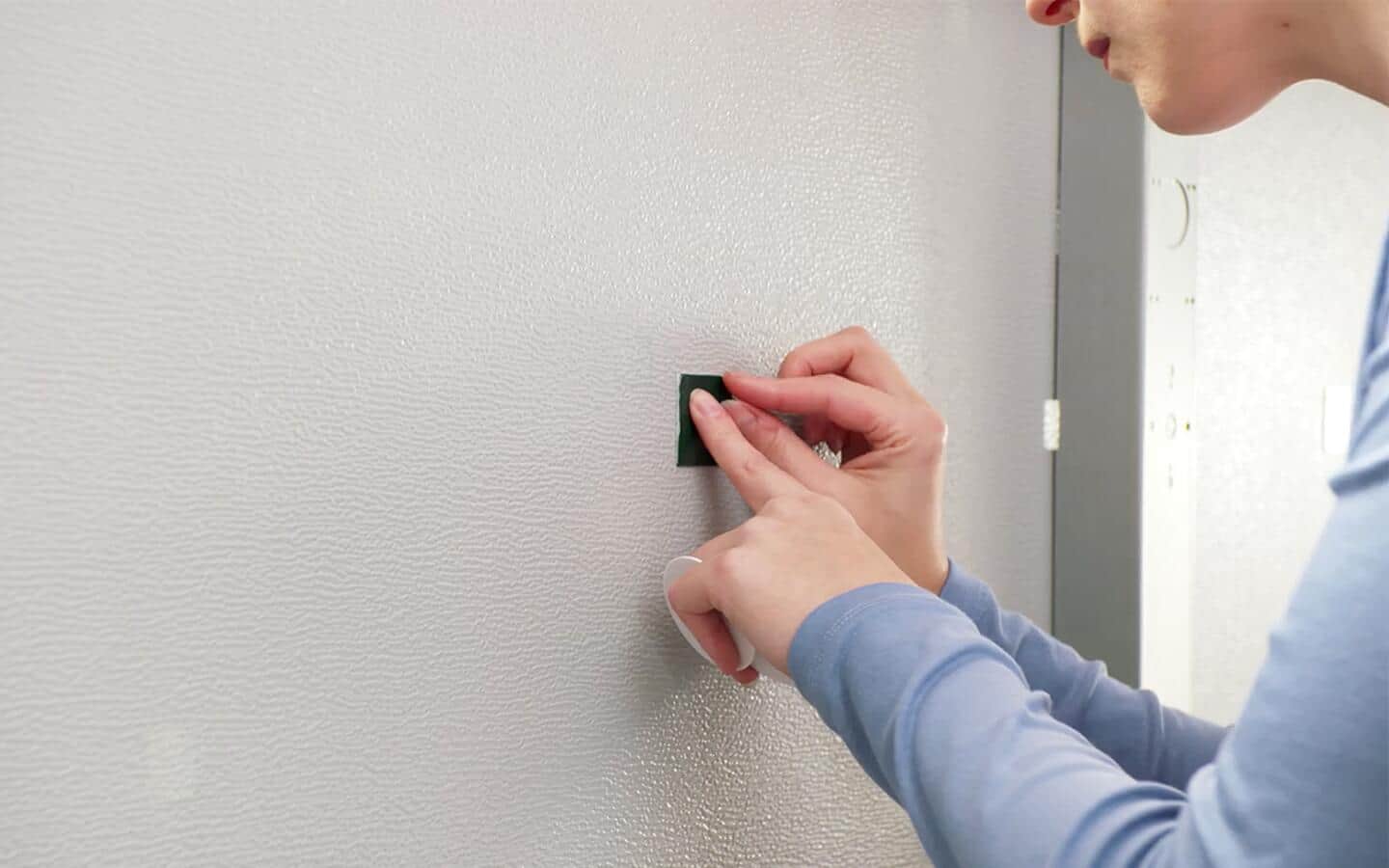 A person placing a piece of double-sided tape on a garage door.