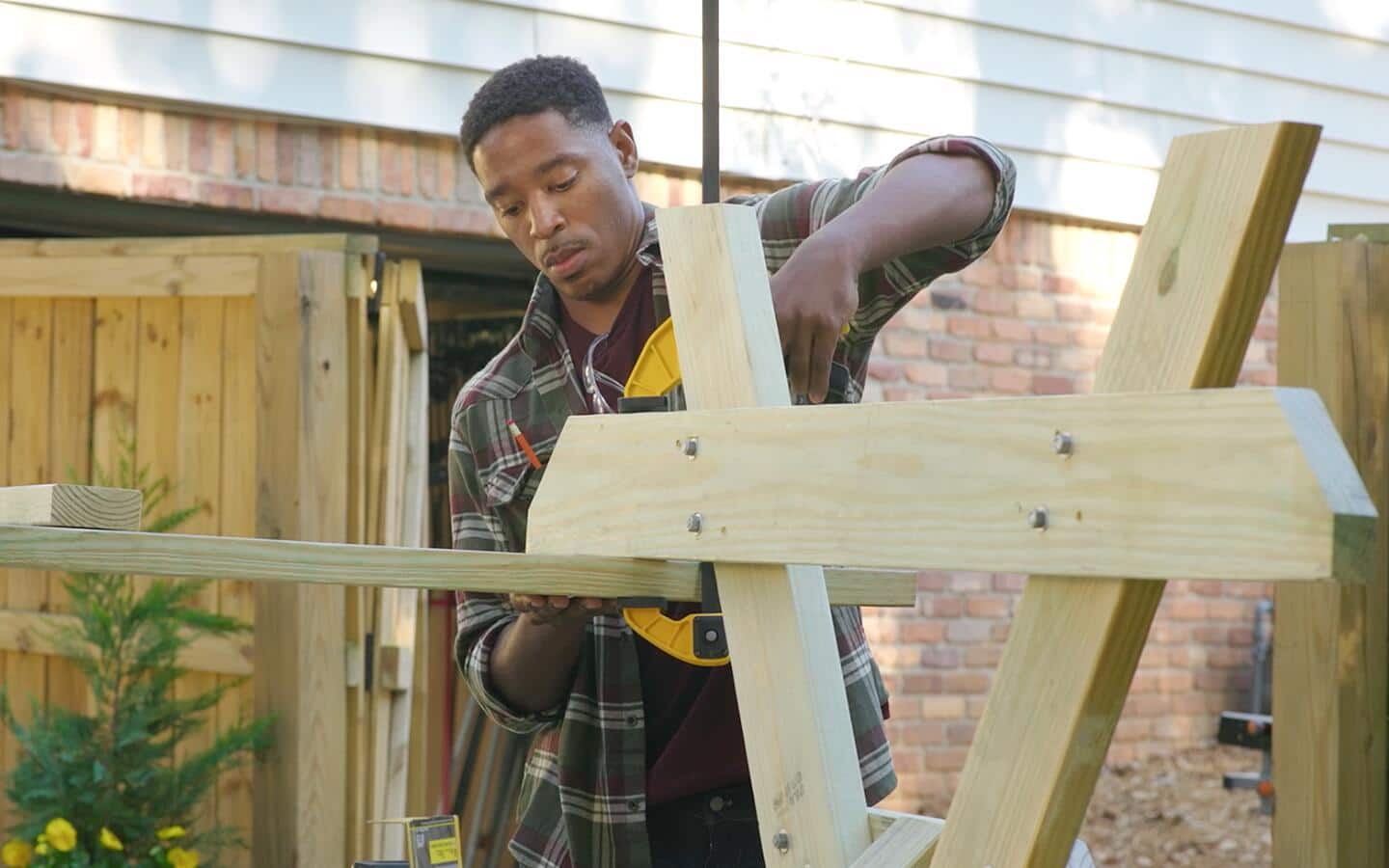 A man uses a woodworking clamp to help attach a bench to a picnic table. A man uses a woodworking clamp to help attach a bench to a picnic table.