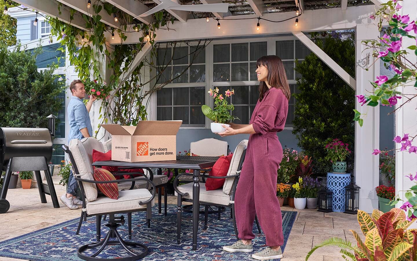Various plants and vines accent a patio, including dining chairs and a table, on a paisley outdoor rug.