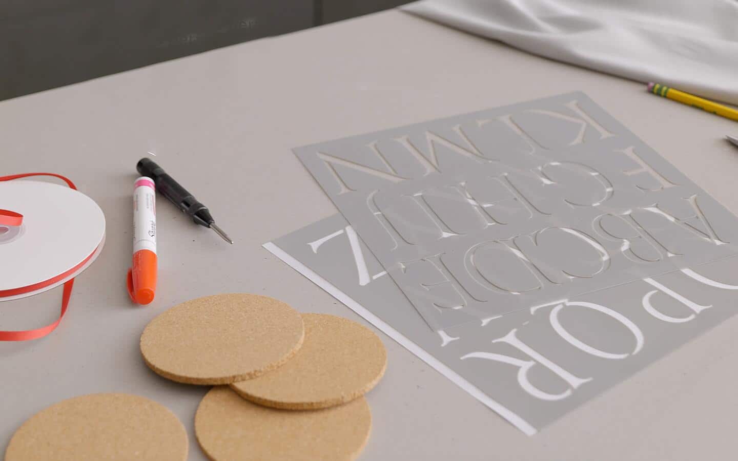 Cork coasters, stencils and an orange marker sit on a counter.