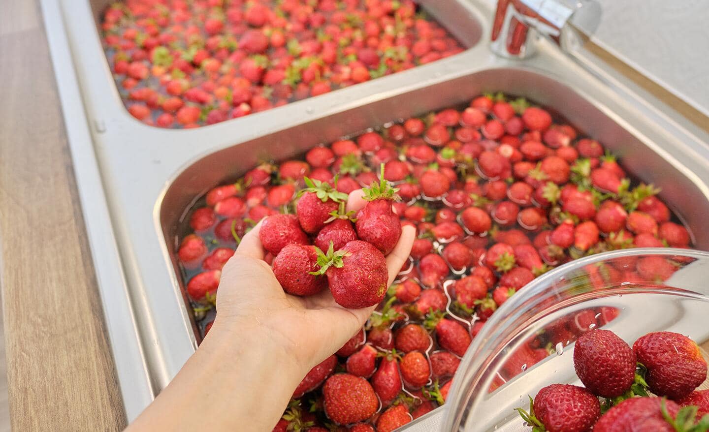 Person holds a handful of strawberries over a sink full of berries in water
