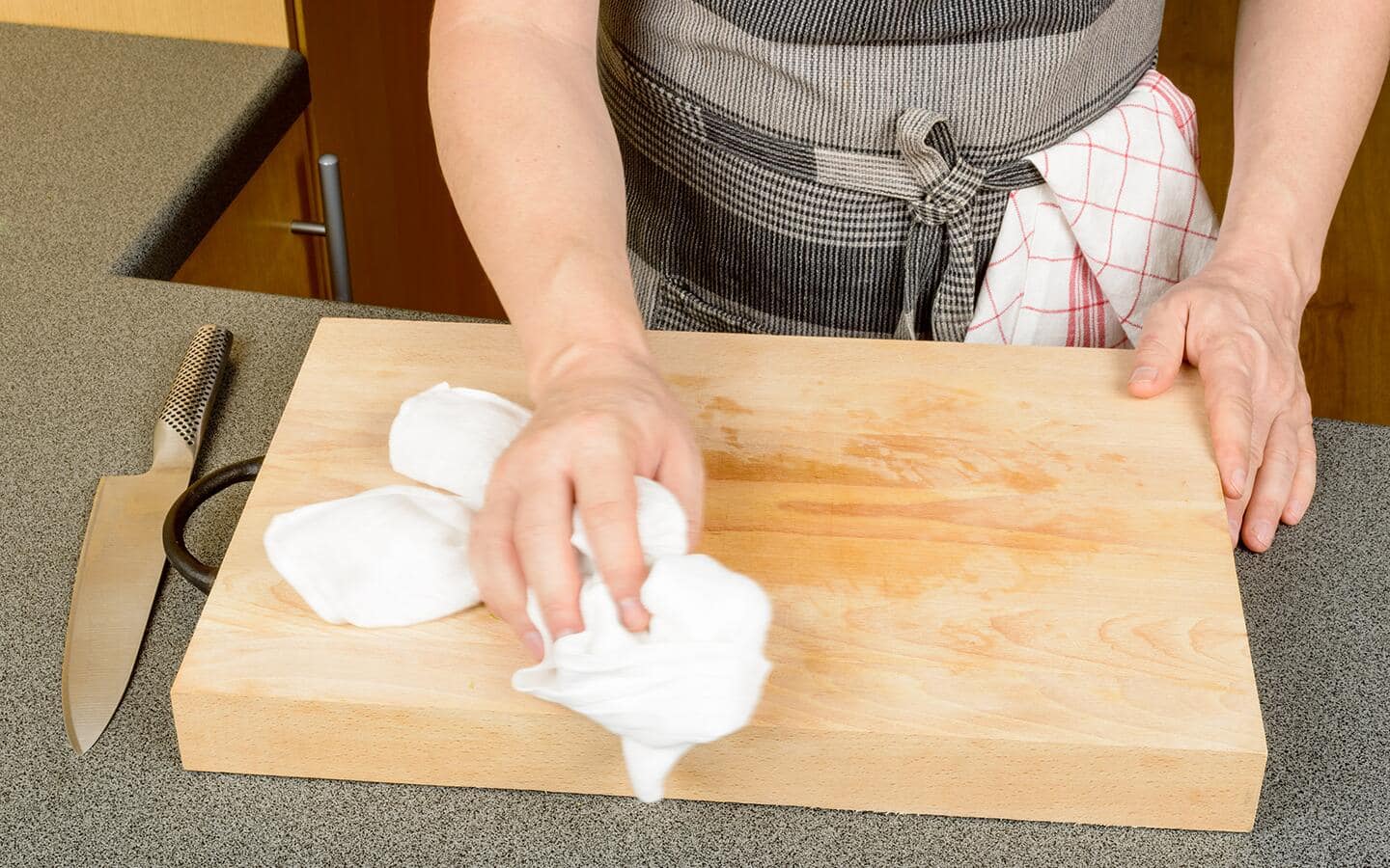 A person wipes a thick wooden cutting board with a cloth. A person wipes a thick wooden cutting board with a cloth.