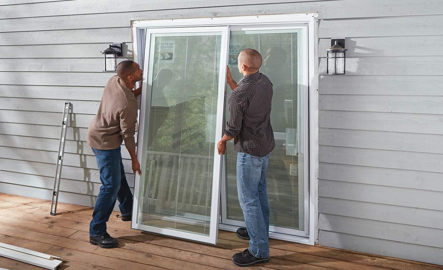 Two people stand on a deck to position a new sliding door in a frame opening.