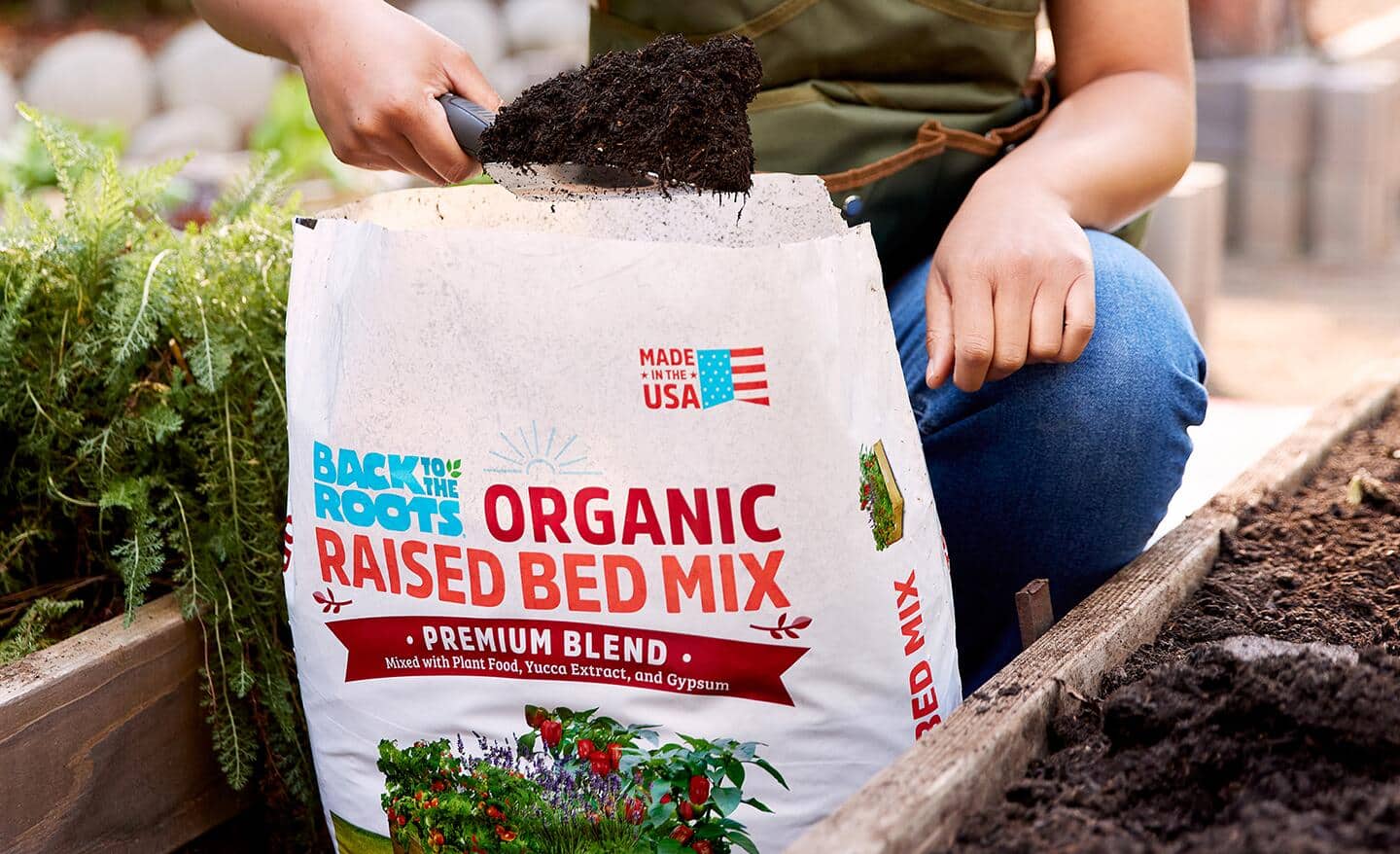A gardener pulls a small shovel of raised bed soil out of a bag.