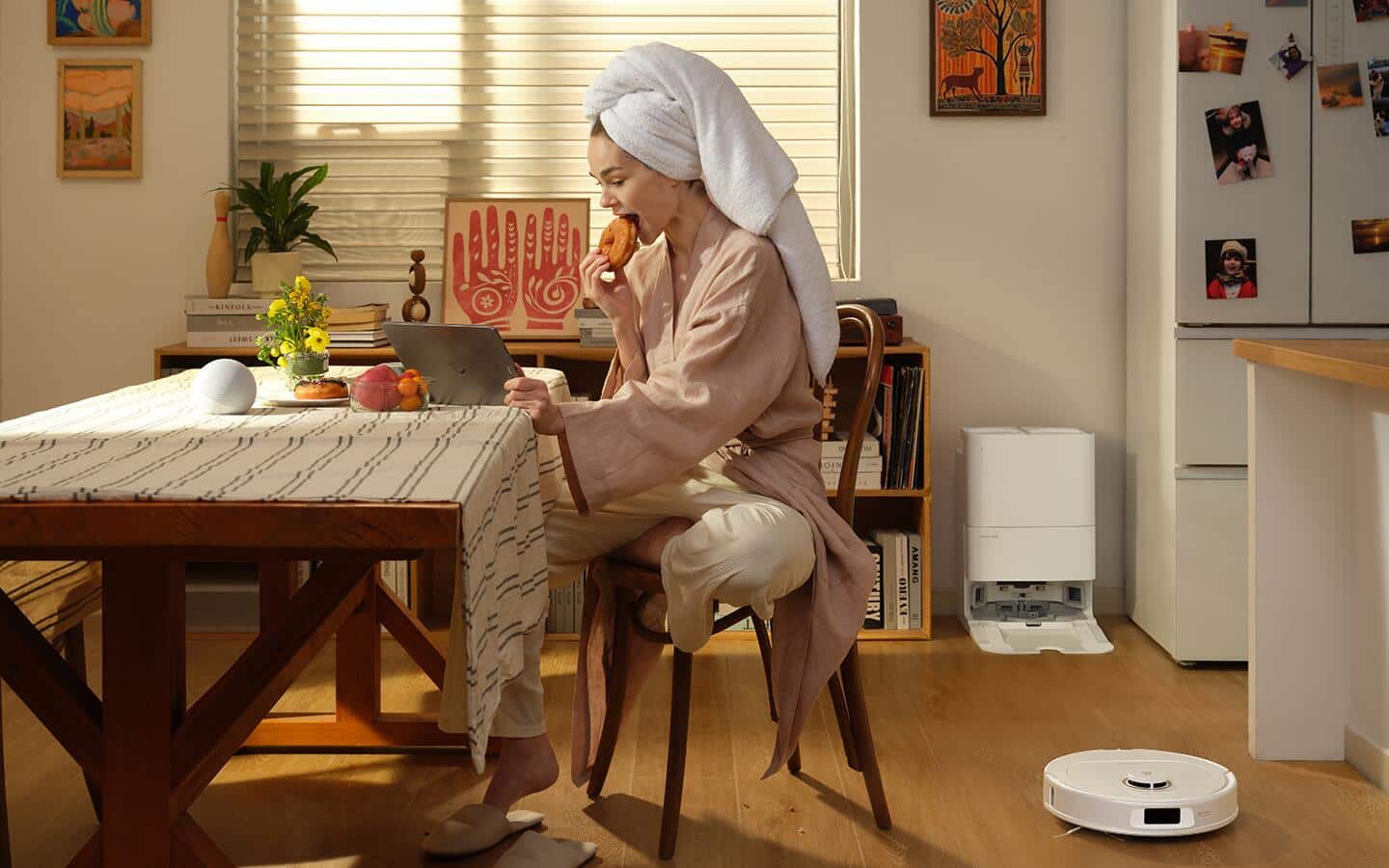 A robotic vacuum cleans a kitchen floor while someone relaxes at a dining table. A robotic vacuum cleans a kitchen floor while someone relaxes at a dining table.