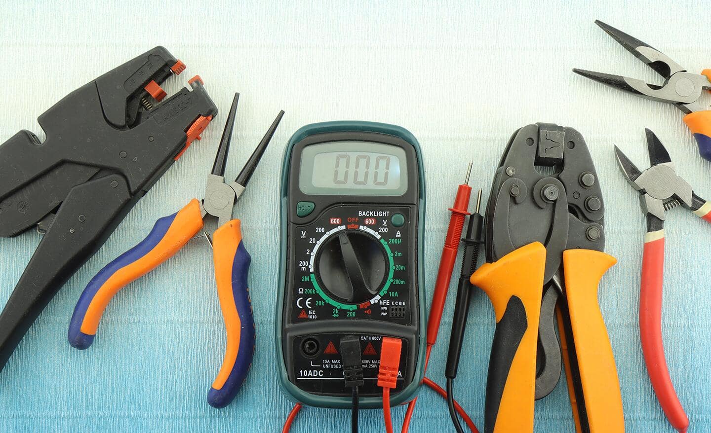 A voltage meter, pliers and other tools gathered on a table.