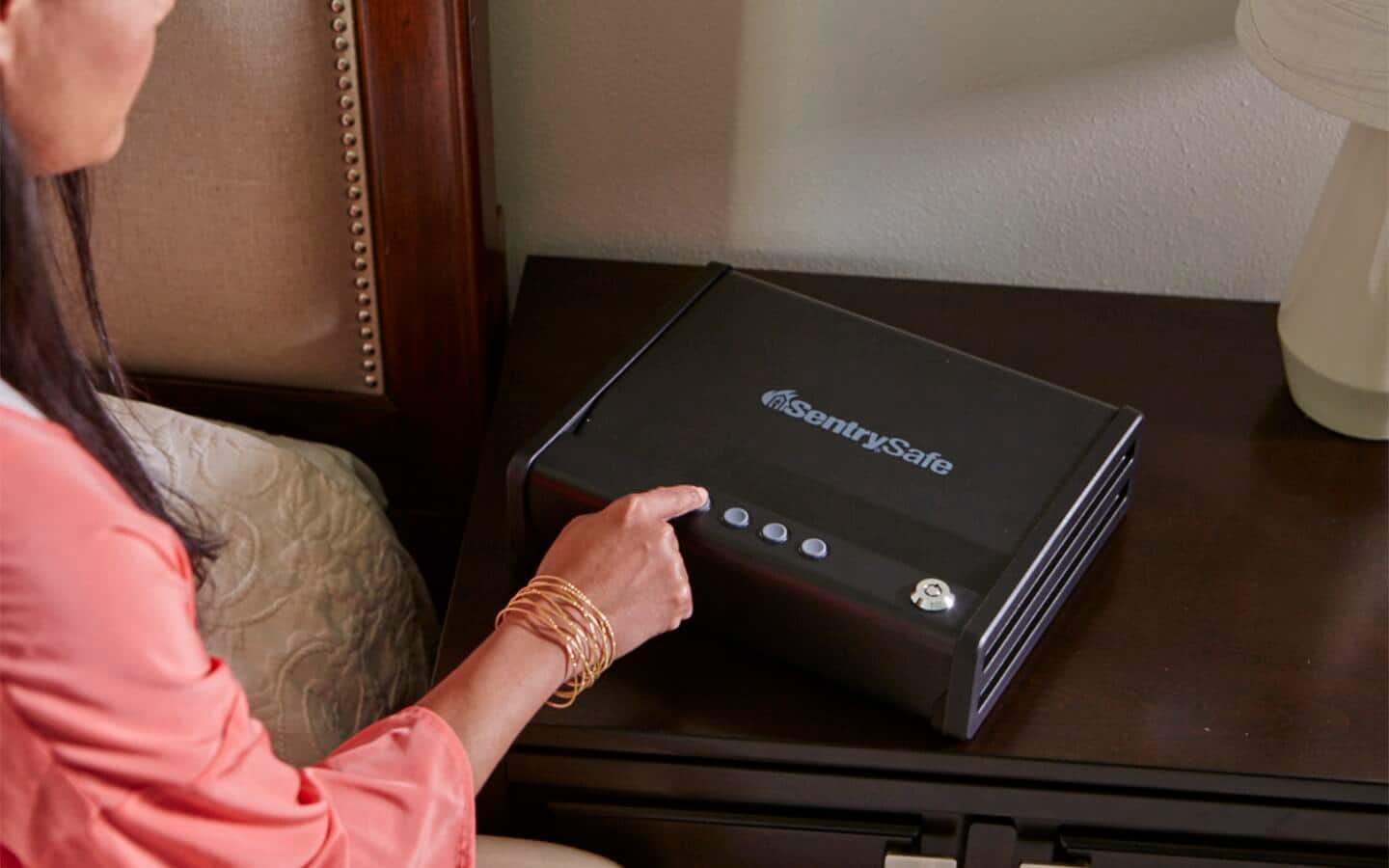 An individual touching a button to lock a gun safe beside a bed.