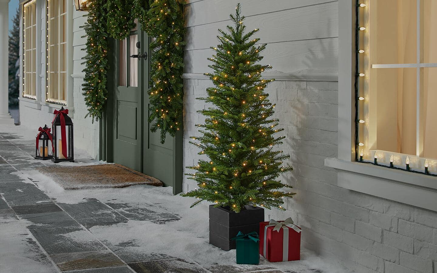 A prelit Christmas tree and matching garland displayed on a front porch. A prelit Christmas tree and matching garland displayed on a front porch.