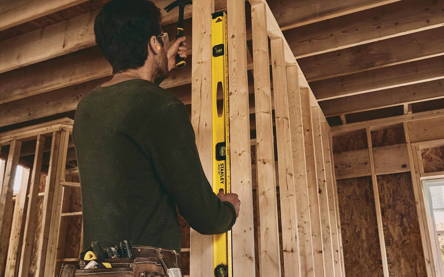 A man using a carpenter's level to mark where to hammer wood. A man using a carpenter's level to mark where to hammer wood.