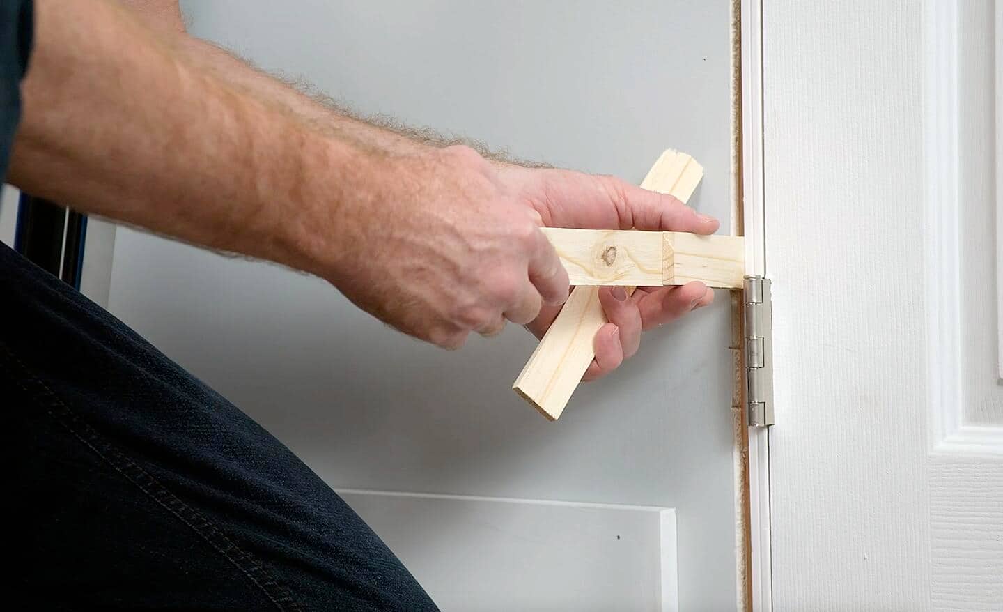 A person leveling a prehung door with shims.