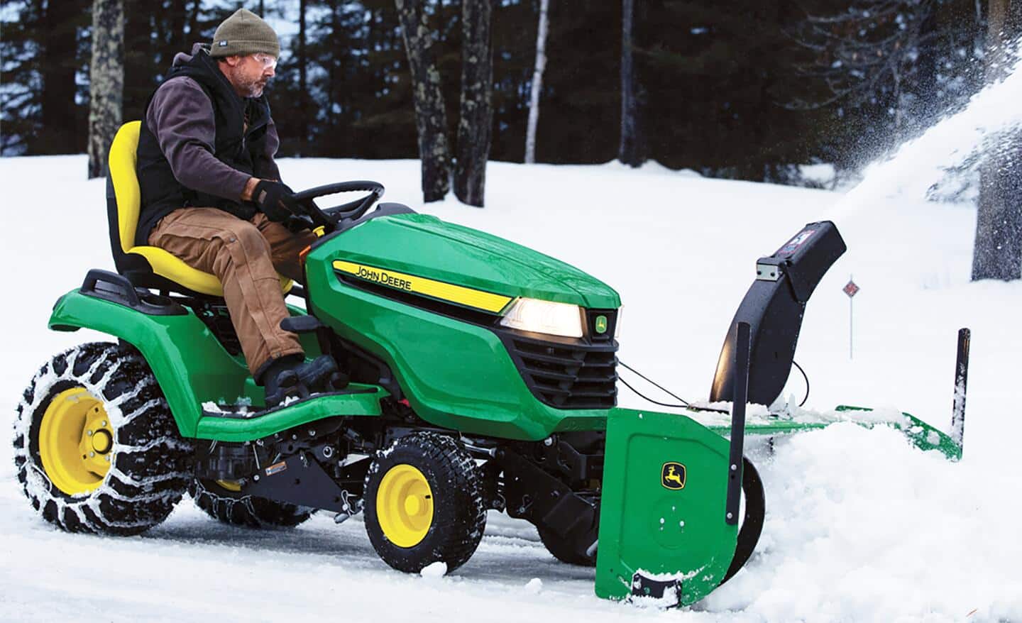 A person uses a riding mower with a snow plow attachment to remove snow.