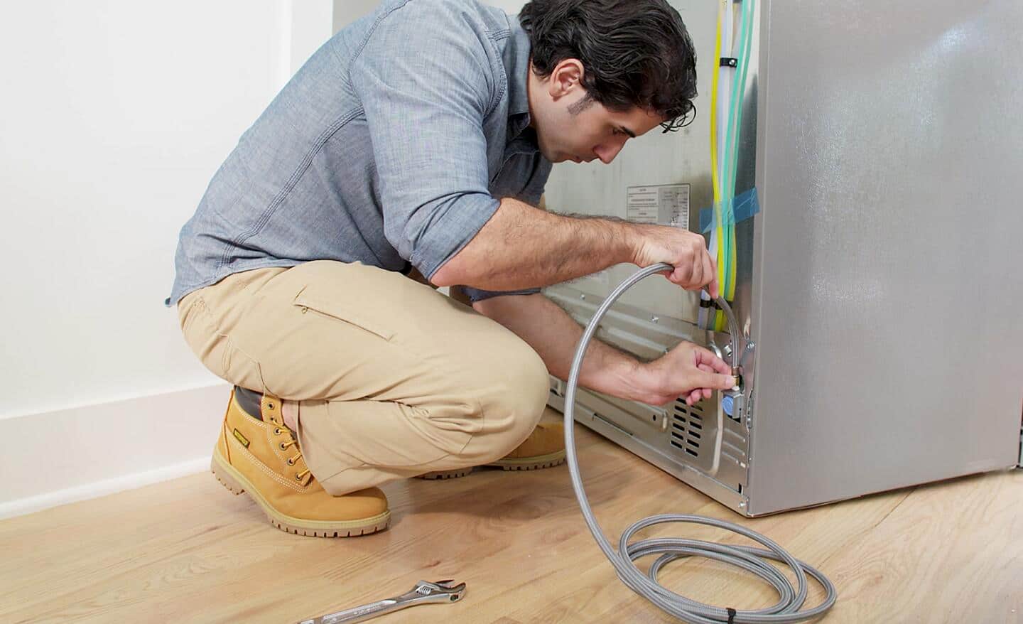 A person connecting a water line to a refrigerator.