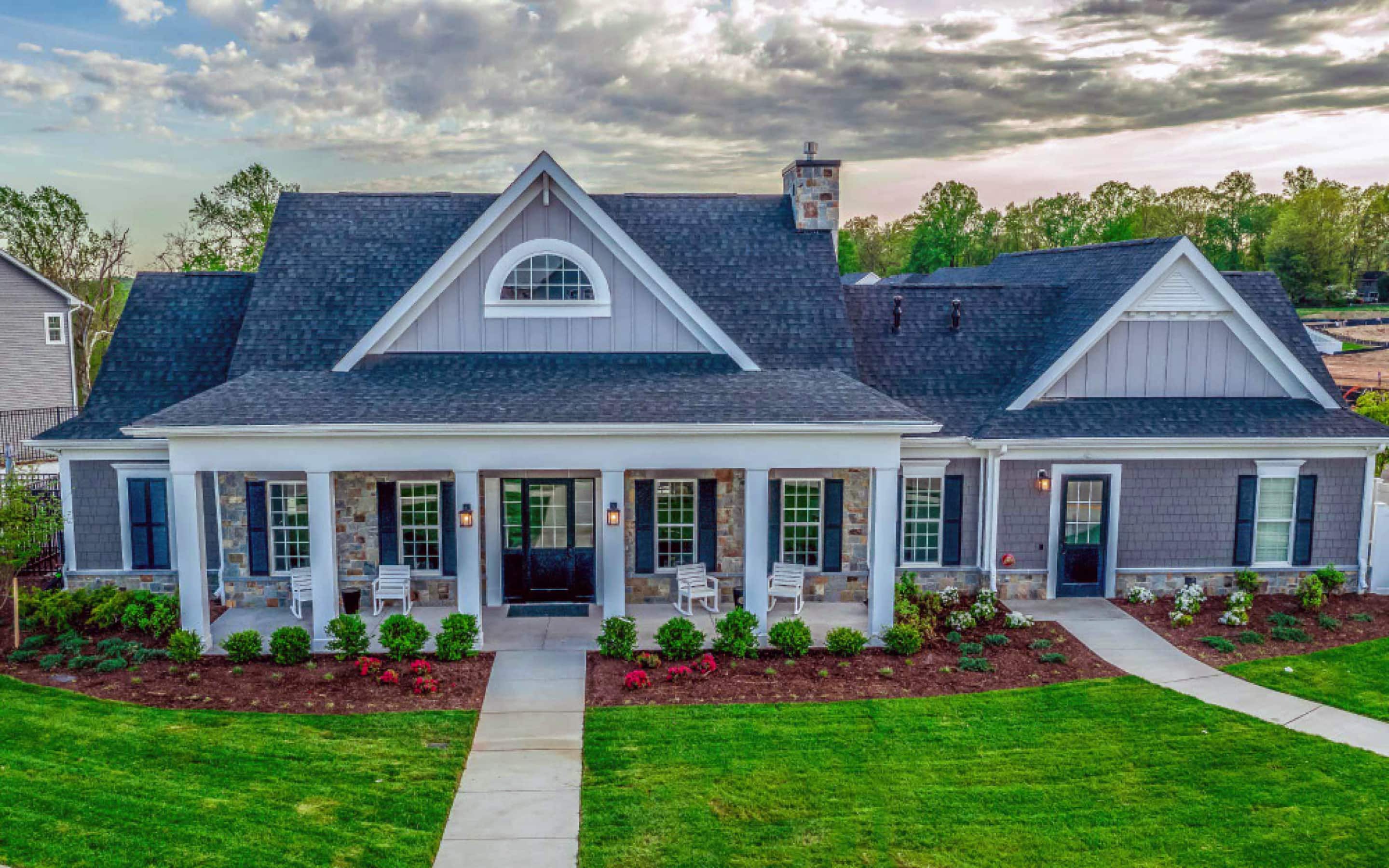 Residential house with a gable roof featuring gray asphalt shingles, a decorative pediment, and a porch with white columns and a natural stone finish.