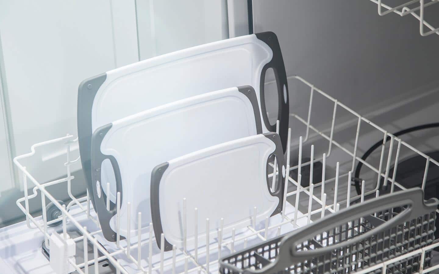 Three white plastic cutting boards stand in the rack of a dishwasher. Three white plastic cutting boards stand in the rack of a dishwasher.