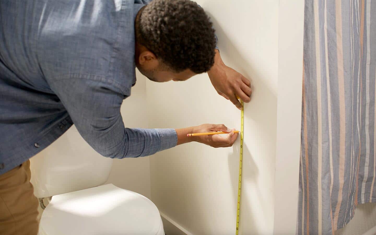 A person measures the height for a toilet paper holder.