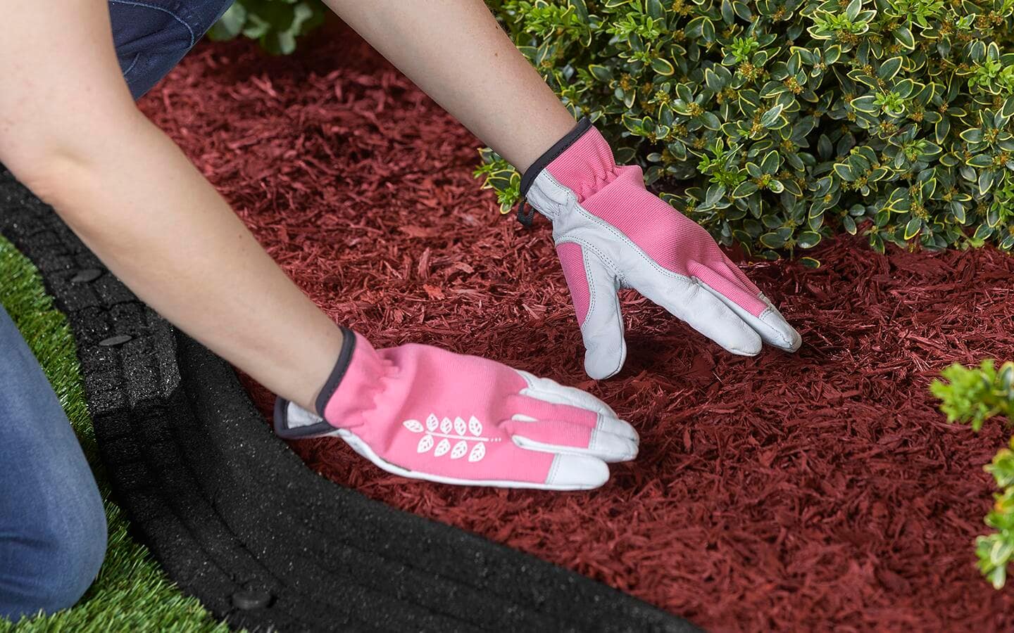 A person in pink work gloves packing down red mulch in a garden. A person in pink work gloves packing down red mulch in a garden.