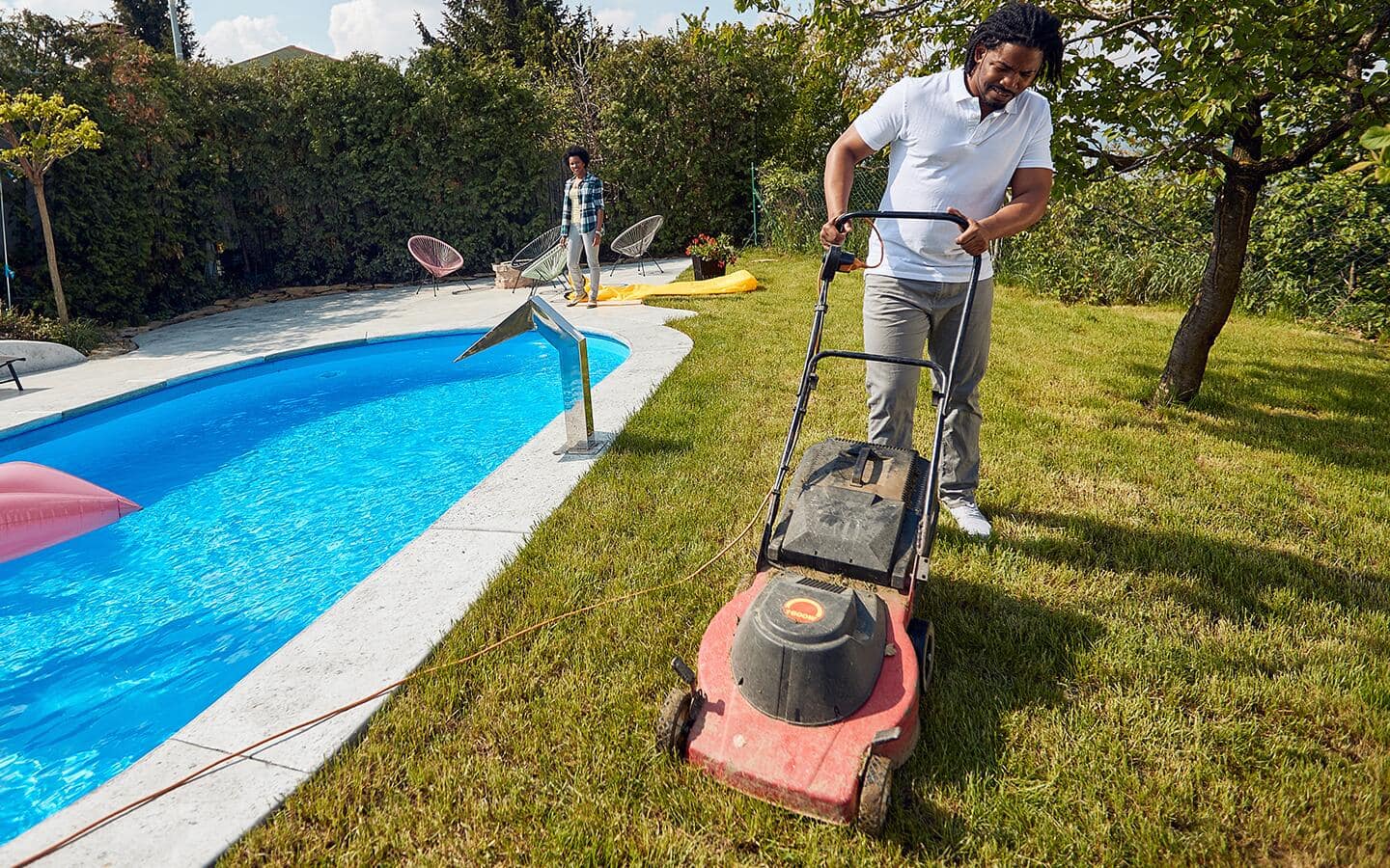 A corded electric lawn mower is being used near a swimming pool.