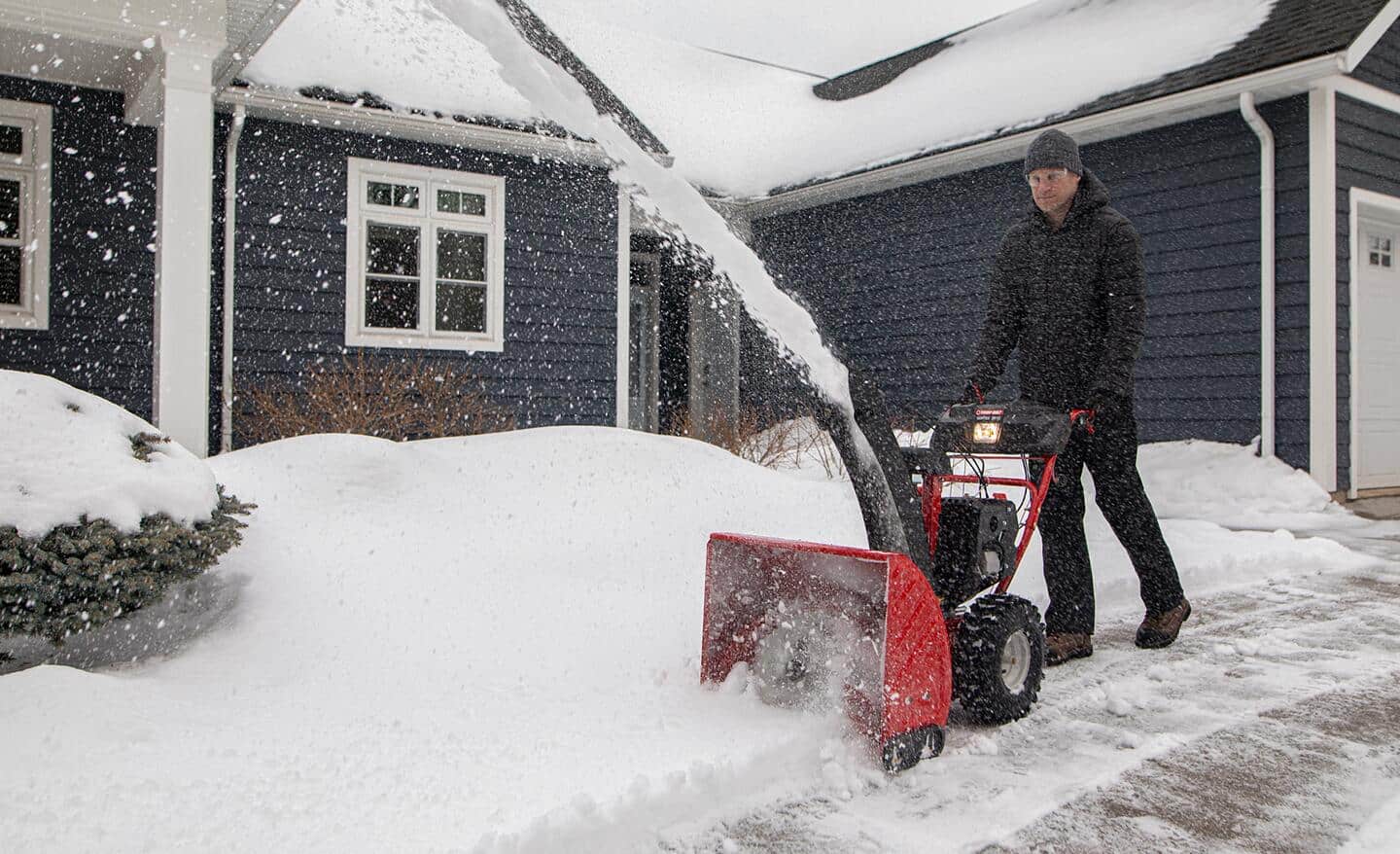 A person clearing a walkway in front of a home with a red three-stage snow blower.