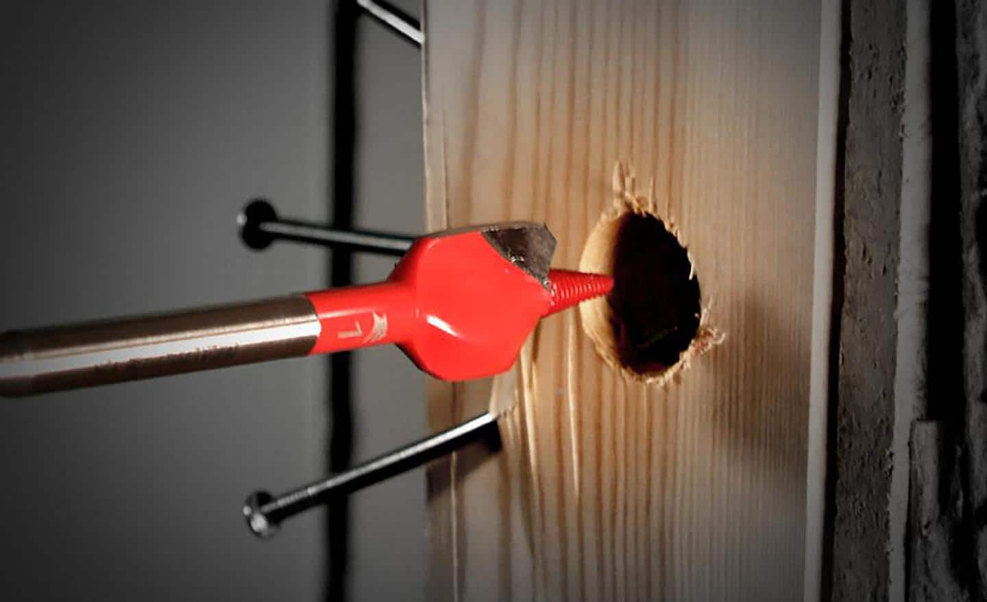 A red spade drill bit being used to drill into wood. 