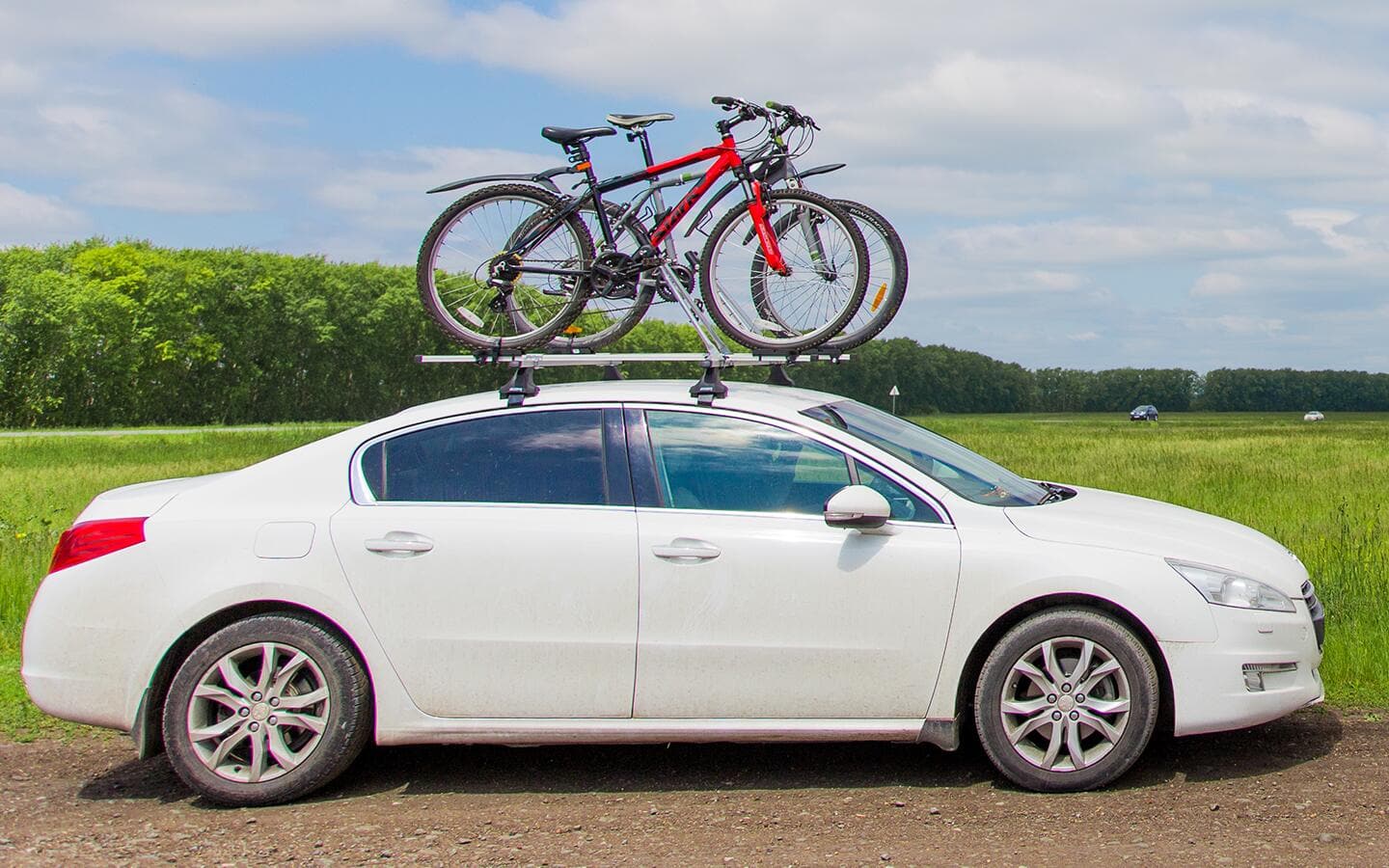A white car features a roof-mounted bike rack with two bicycles.