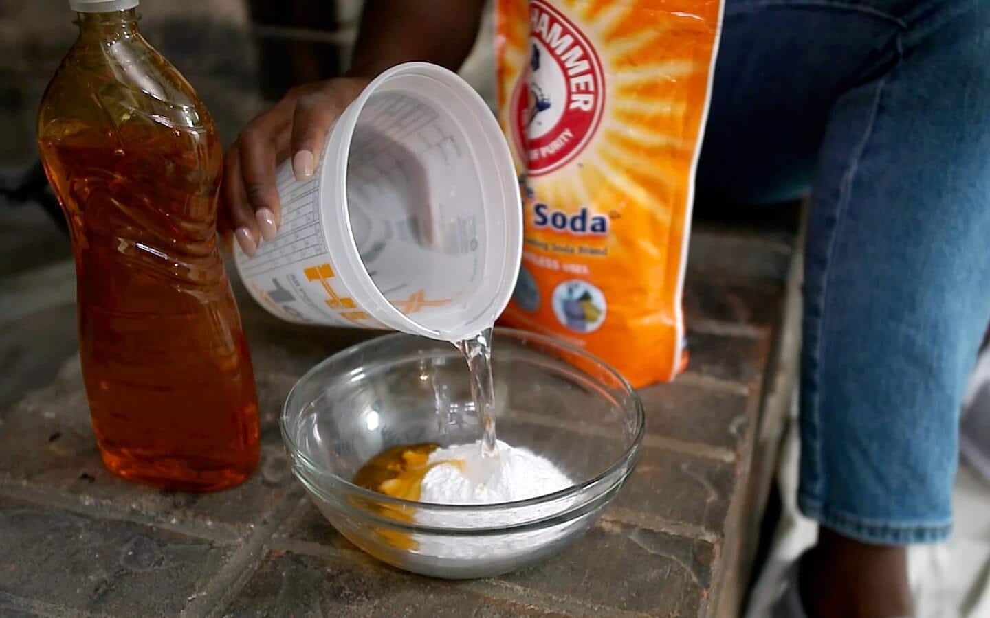 A person pours water into a bowl of baking soda and dish soap.