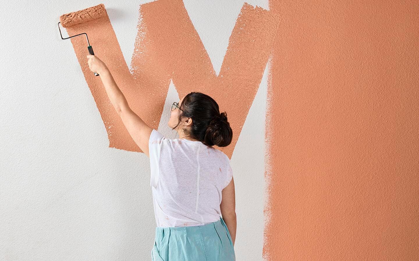 Someone painting a large wall with orange paint.