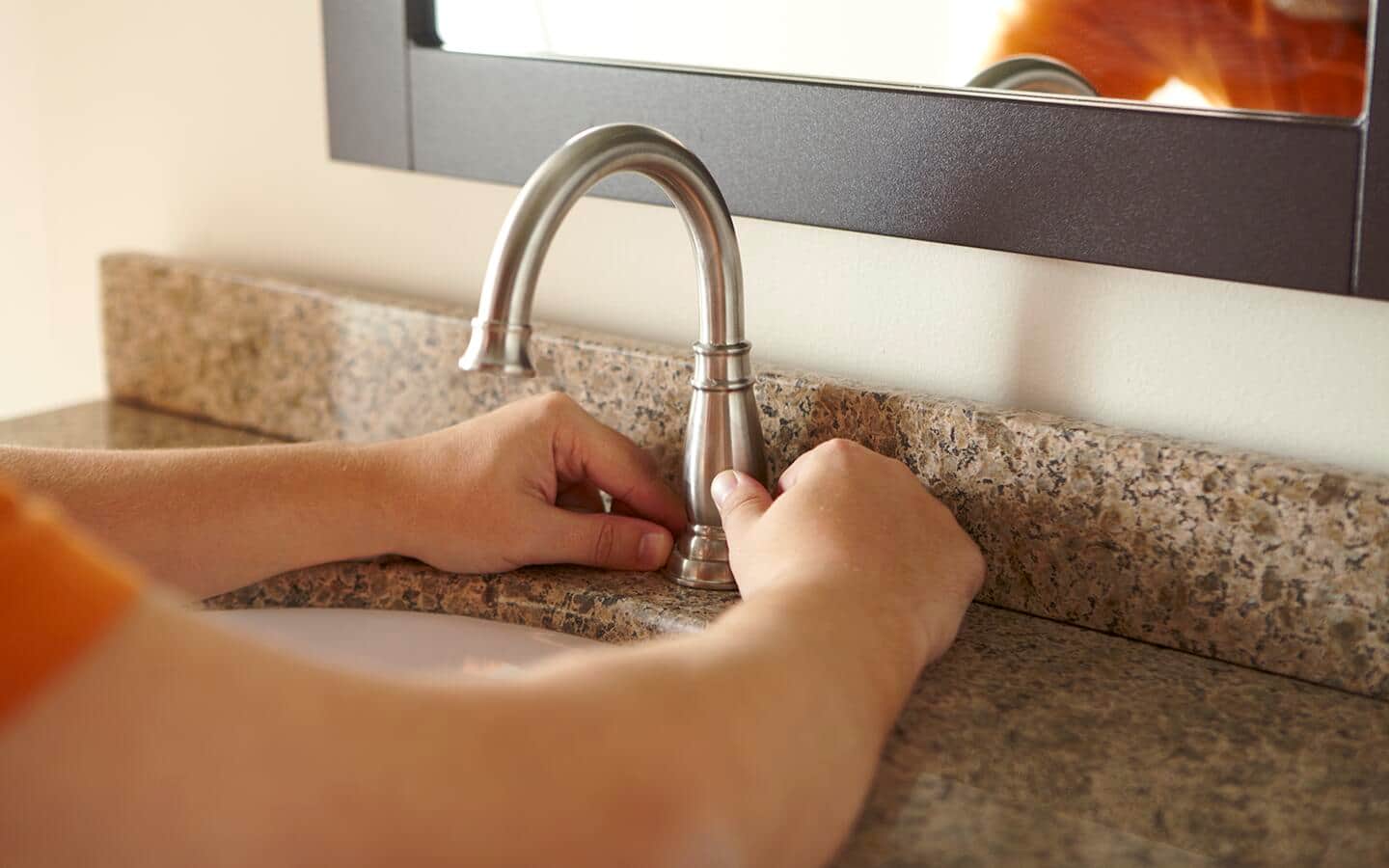 An individual installing a sink faucet onto a vanity beneath a mirror. An individual installing a sink faucet onto a vanity beneath a mirror.