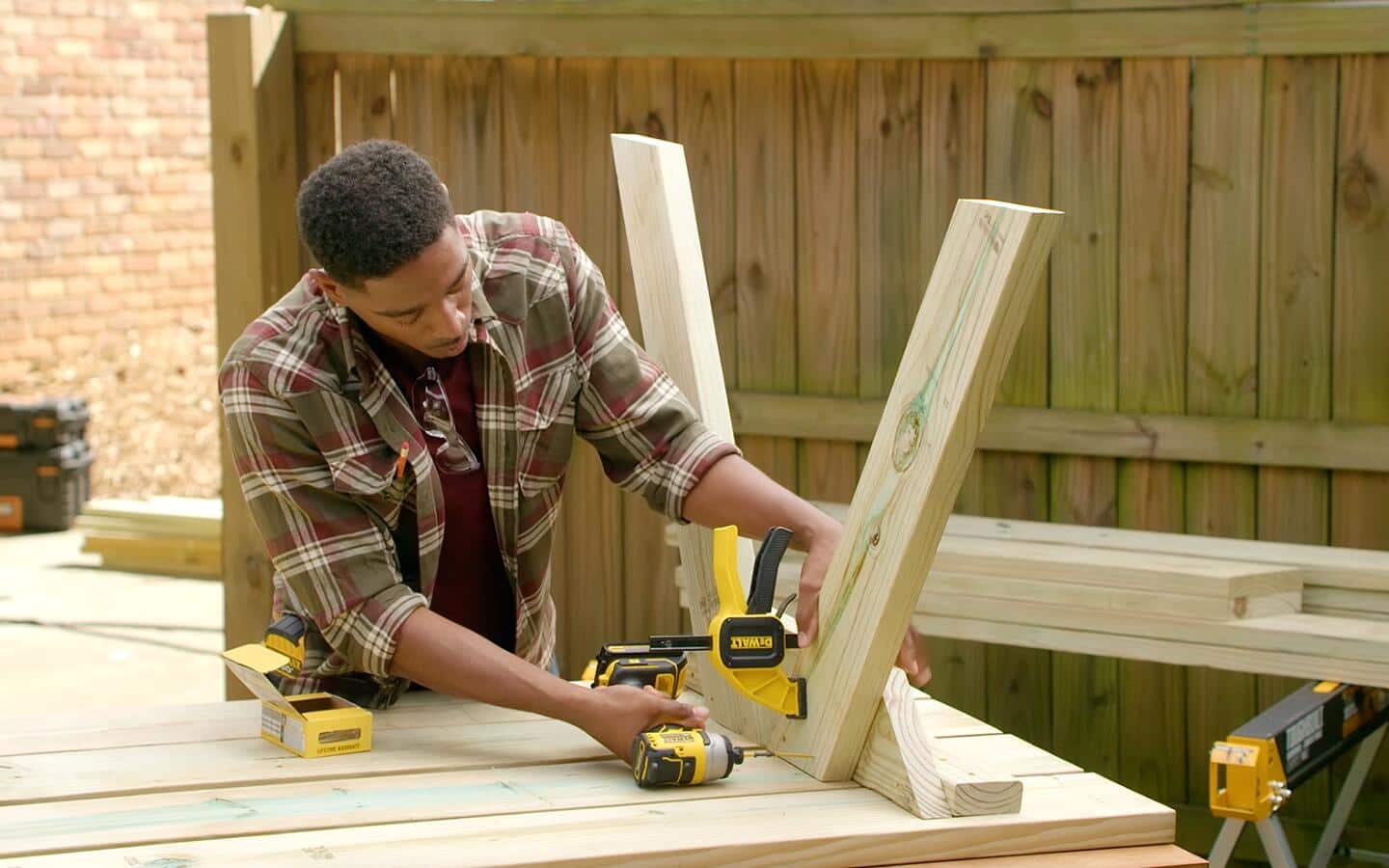 A man attaches angled legs to a picnic table using coated deck screws and a battery powered impact driver. A man attaches angled legs to a picnic table using coated deck screws and a battery powered impact driver.