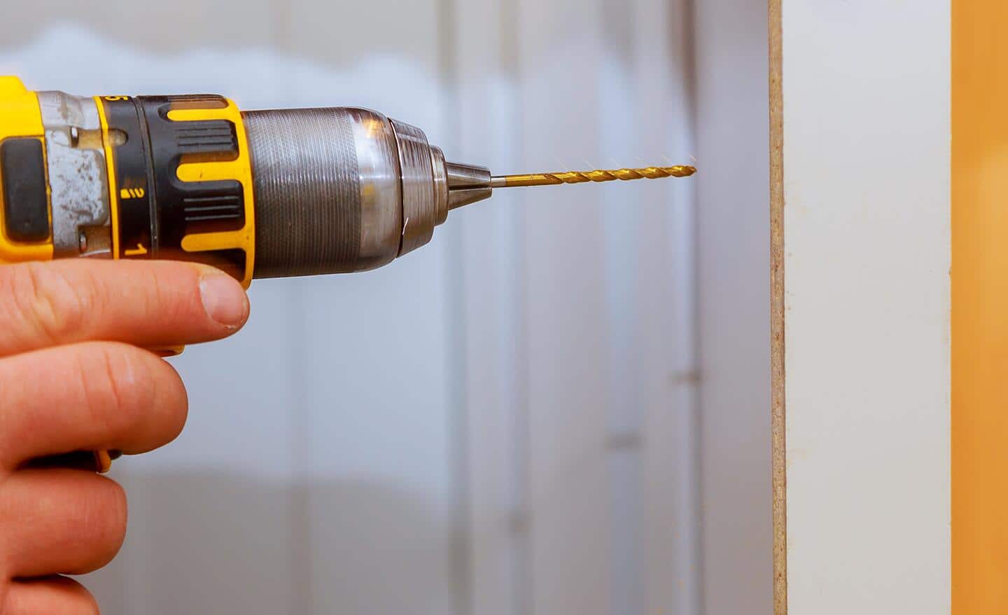 A person drills a screw into a cabinet.