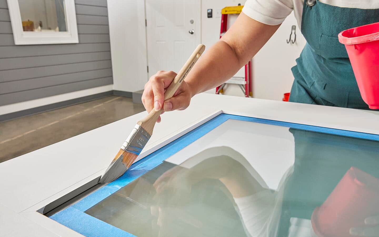A door with a glass window has been masked with painter's tape and is being painted with a cut-in brush. A door with a glass window has been masked with painter's tape and is being painted with a cut-in brush.