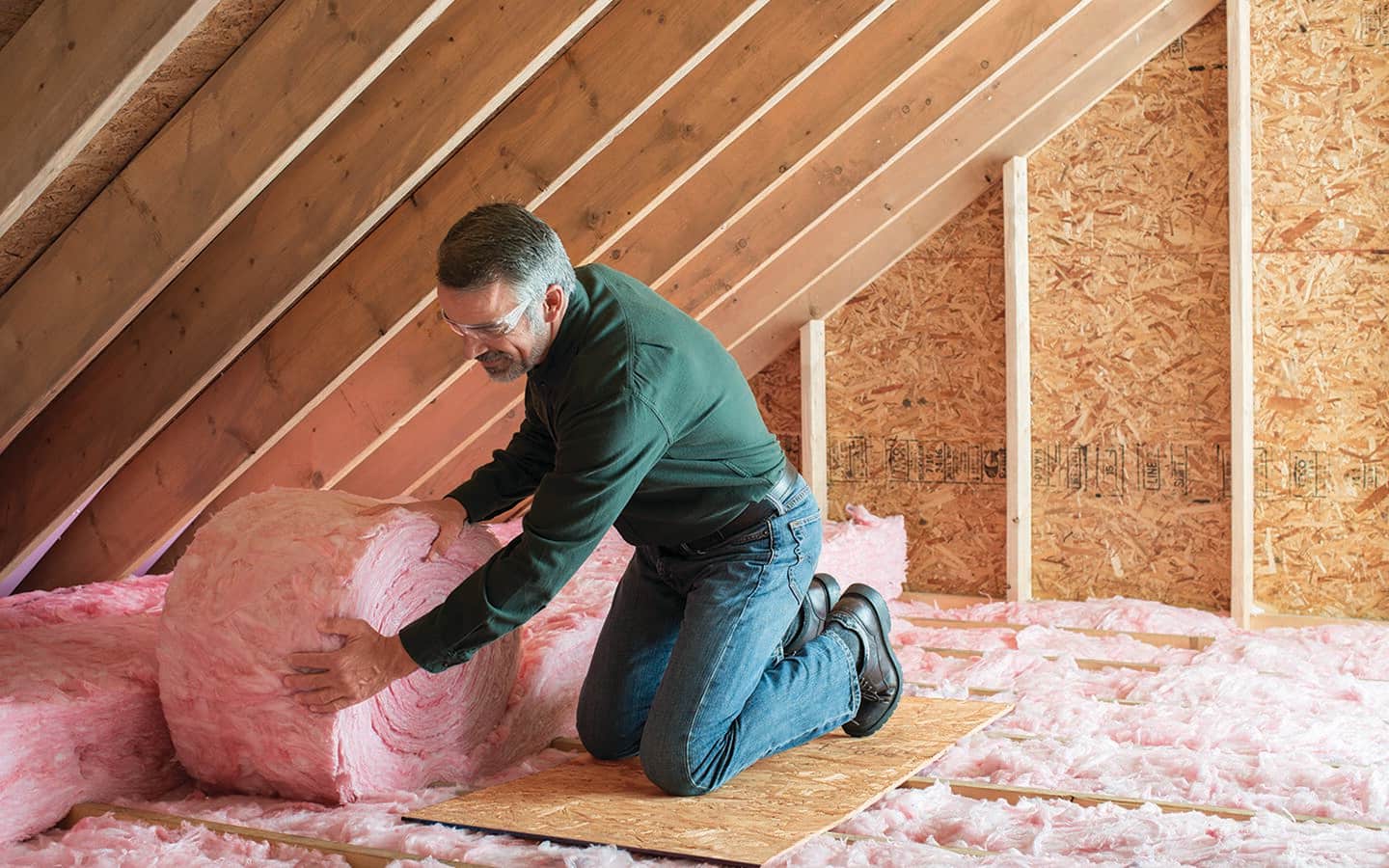 A man installs rolled insulation in an attic. A man installs rolled insulation in an attic.