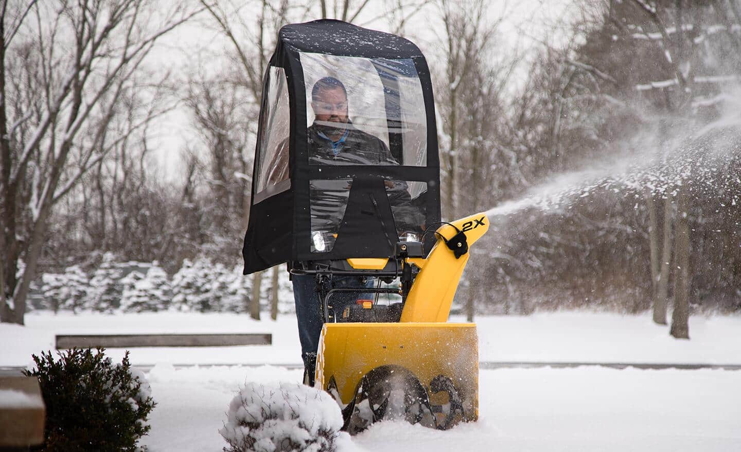 A person using a yellow snowblower with a removable weather cover.