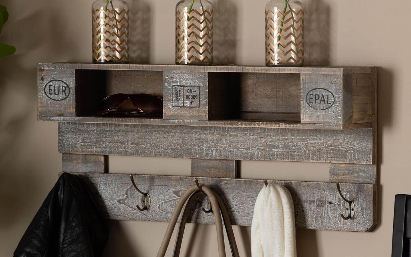 A finished brown wall shelf with hooks holding candles, clothing and other items.