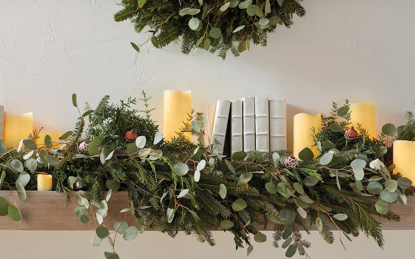 A fireplace mantel decked with fresh greenery and candles.