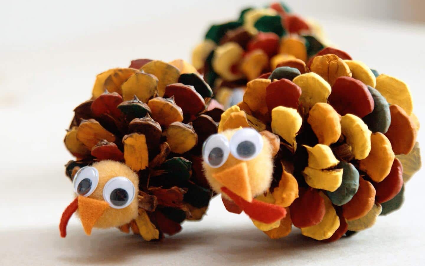 Two colorful turkey pinecones sit on a table.