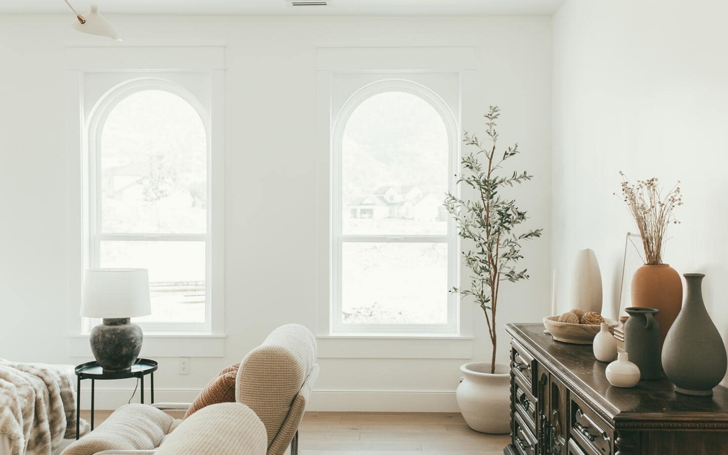 Two tall windows in a living room behind a brown dresser and other furniture.