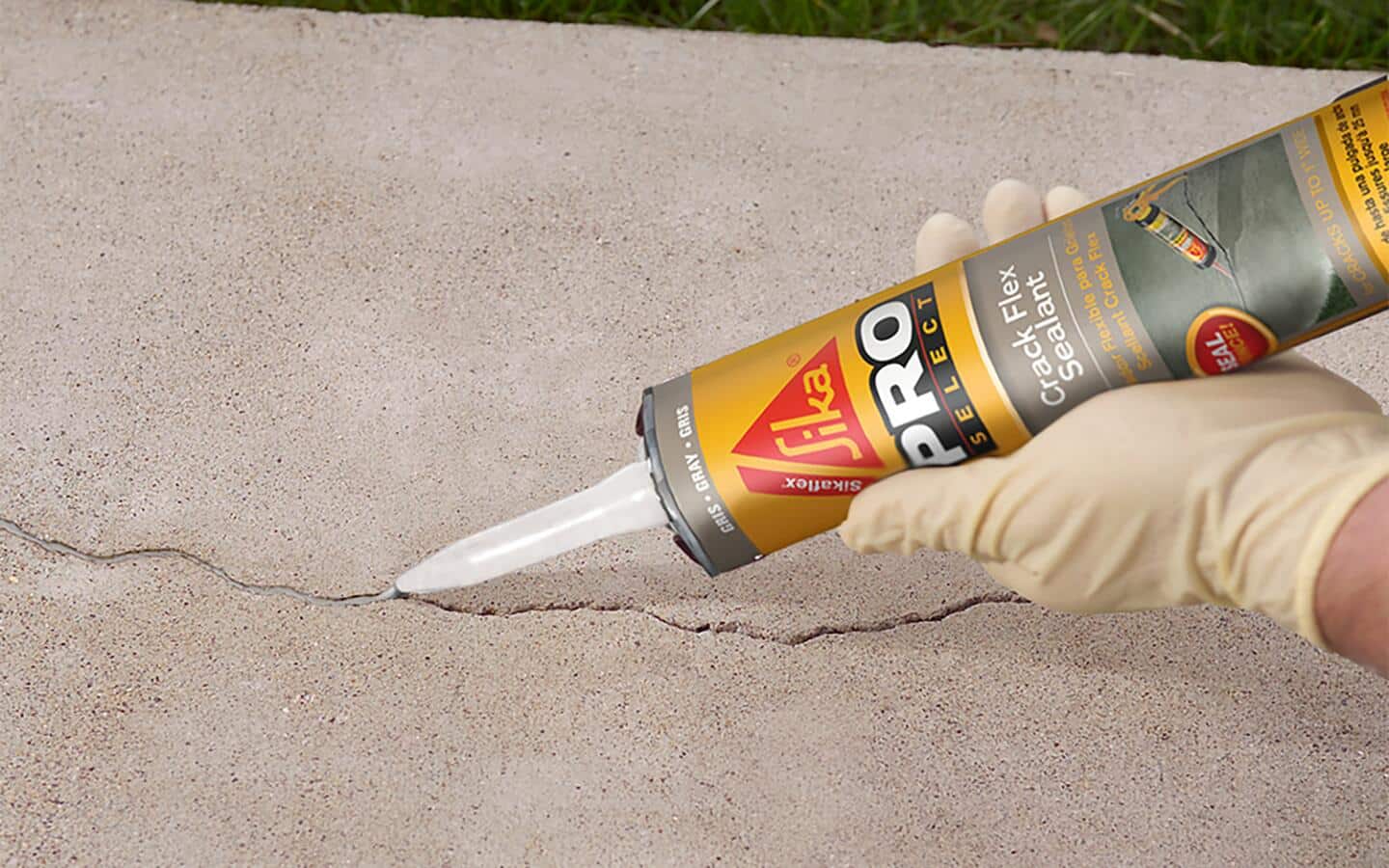 A gloved person applying sealant to a crack in concrete.