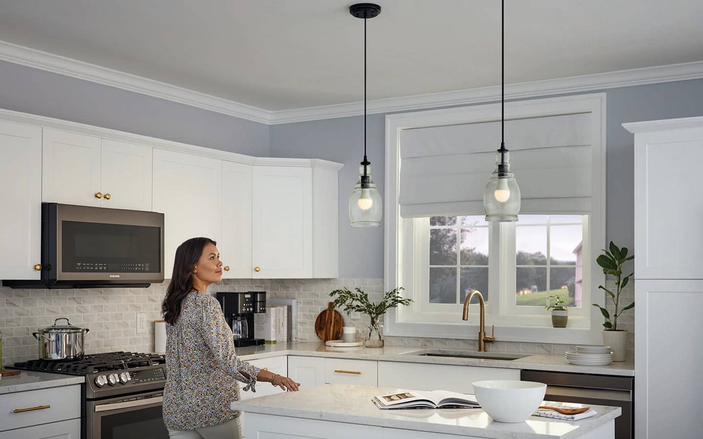 A person in a kitchen admires two hanging lights with energy efficient bulbs. 