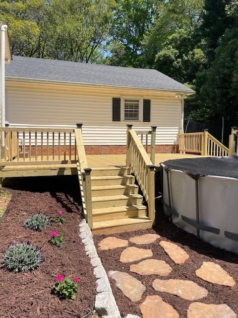  A completed backyard with finished deck, railings, stairs leading to newly installed pavers, and a new garden bed.