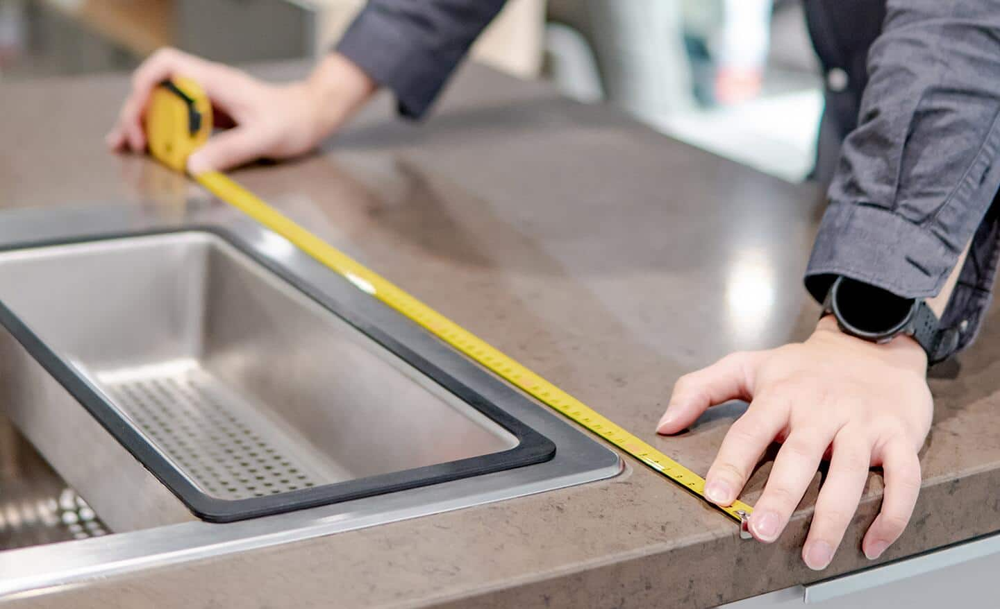 A person measures the width of a sink with a tape measure.