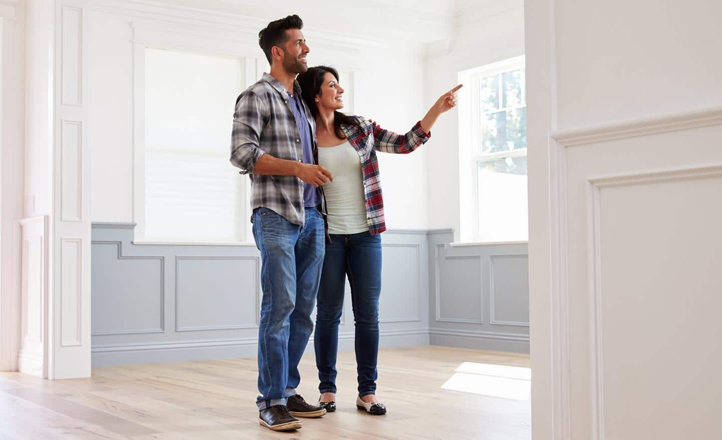 A couple inspecting and pointing at a living room wall.