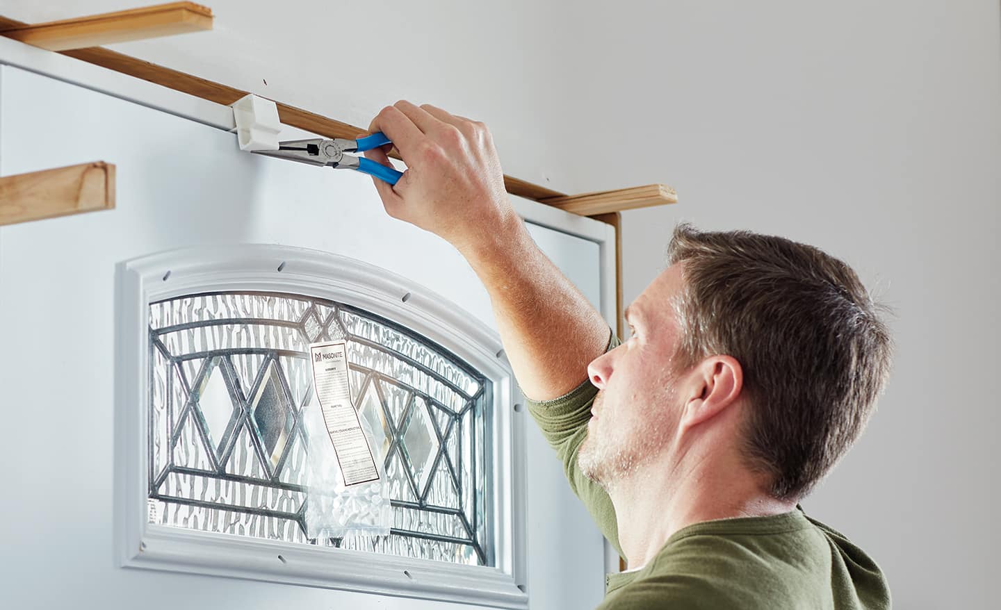 A man applying shims to a new entry door inside the home.