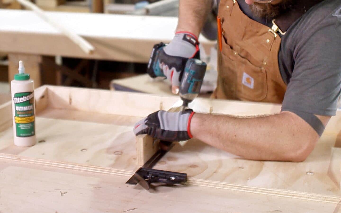 Holes are drilled into plywood piece that serves as the top of a DIY desk.