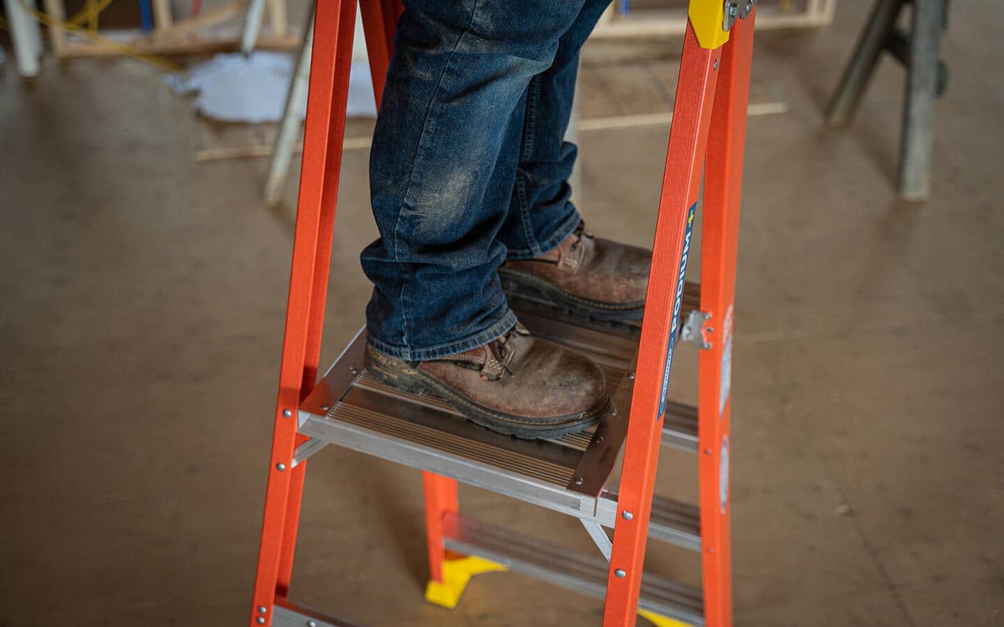 A person, wearing boots, stands on a platform ladder.