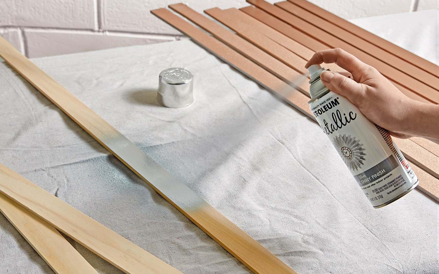 A person spray painting wooden slats with a can of silver paint.