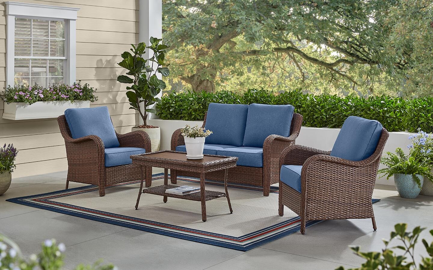 A neutral outdoor rug under a blue sectional sofa and matching ottoman on a patio.