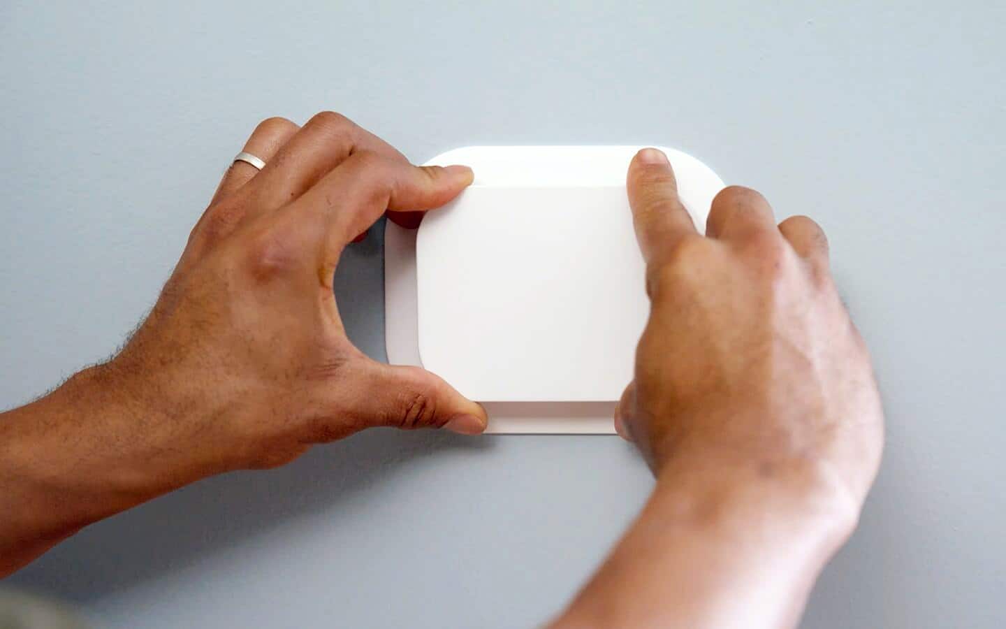 A person installs a smart thermostat on a wall.